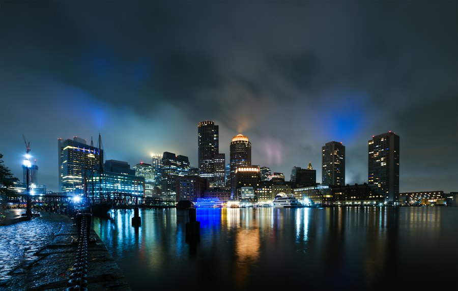 The Boston skyline lit up on a rainy night, reflected in the water